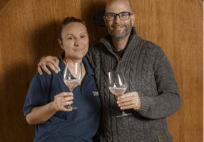 Two people holding wine glasses by barrel